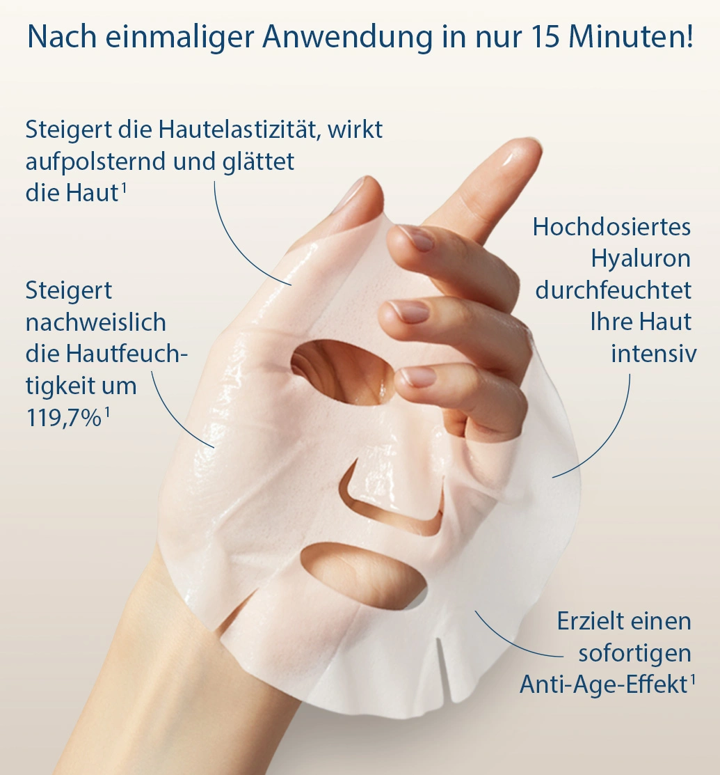 Hand hält eine weiße Gesichtsmaske mit Aussparungen für Augen, Nase und Mund, im Hintergrund die goldfarbene Verpackung.