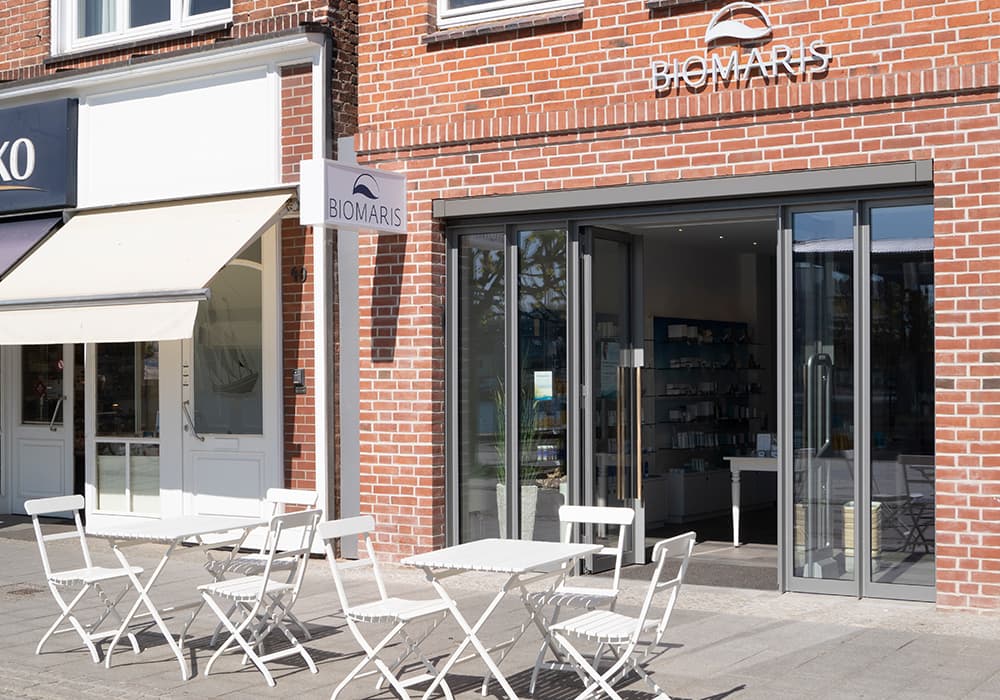 BIOMARIS Shop Travemünde BIOMARIS Shop Eingangsbereich mit Glasfront und weißen Bistrostühlen vor dem Geschäft in rotem Ziegelbau