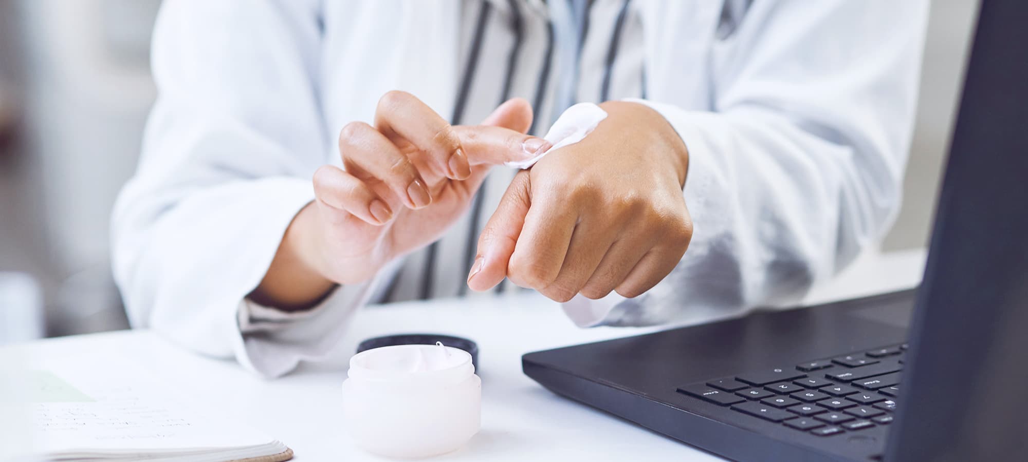 Anwendungstest: Person trägt Creme auf Hand auf, Laptop im Hintergrund