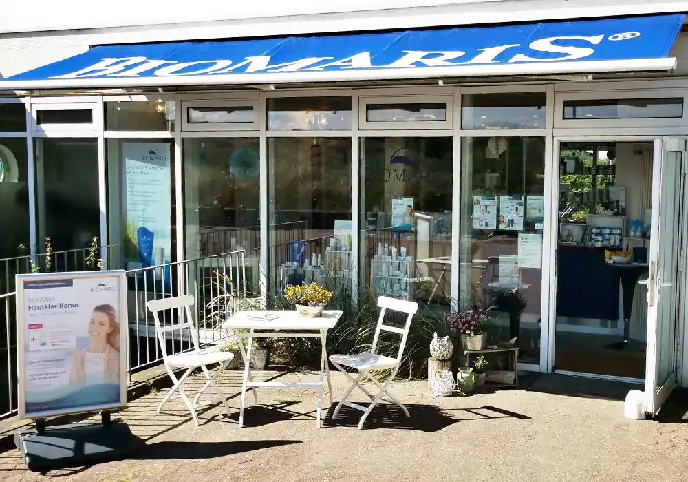 Eingang des BIOMARIS-Shops auf Baltrum mit Werbeschild und Sitzgruppe vor der Glasfassade