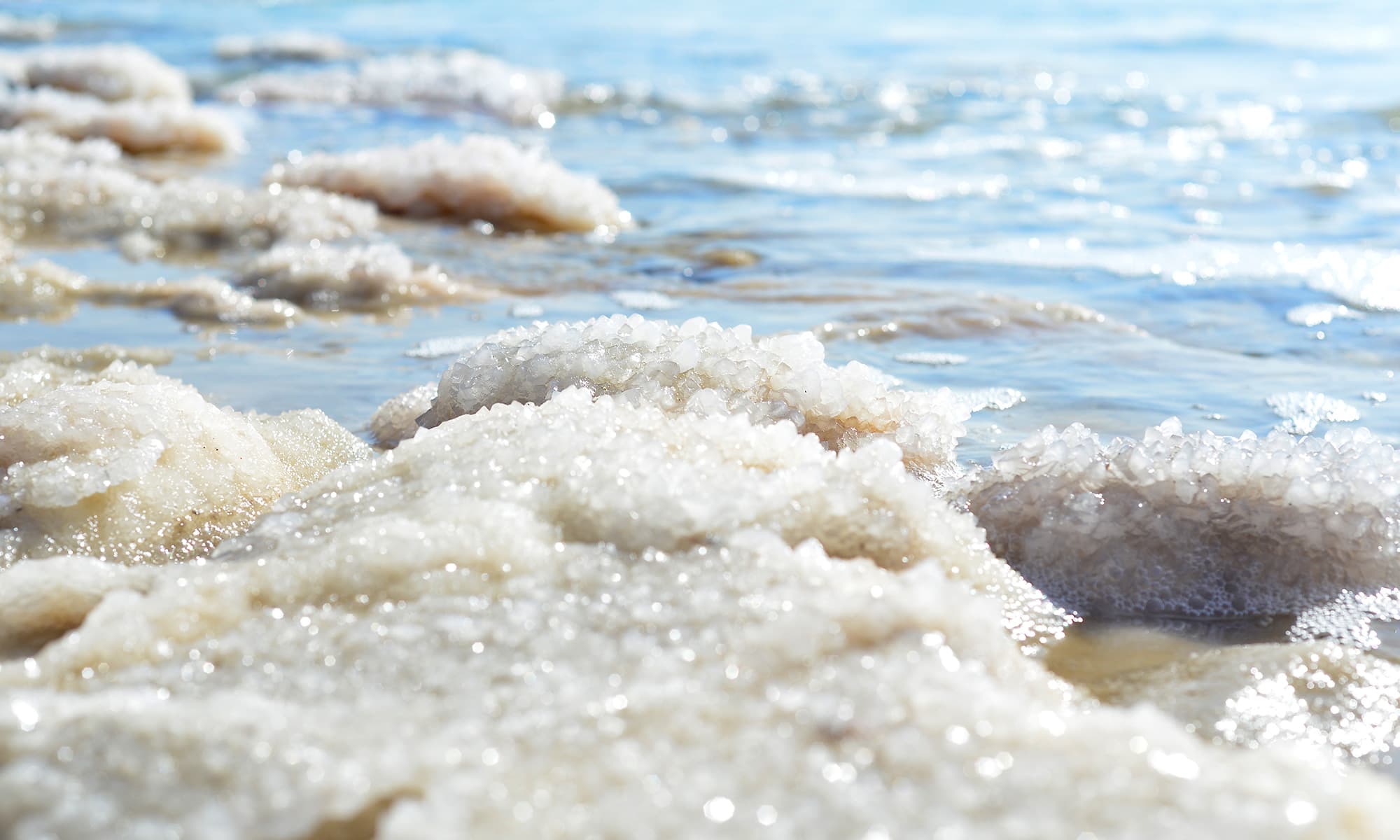 Salzablagerungen an einem Meeresufer mit glitzernden Kristallen und blauem Wasser