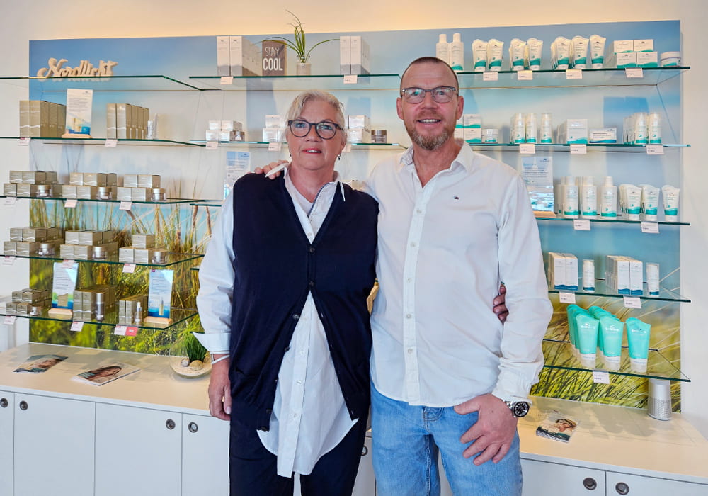 Ein Shop-Betreiber und eine Mitarbeiterin stehen lächelnd vor einem Verkaufsregal mit Biomaris-Produkten im modern gestalteten Laden.