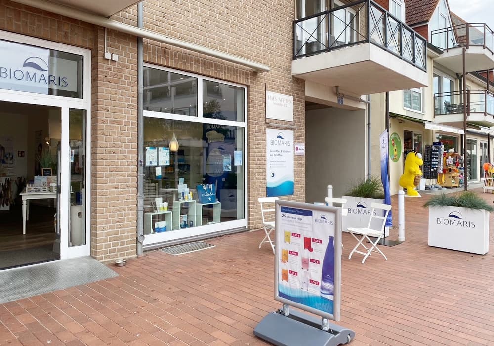 BIOMARIS Shop Scharbeutz Eingang des BIOMARIS Shops Scharbeutz mit Werbetafel und Sitzgelegenheit auf rotem Pflaster in Einkaufsstraße