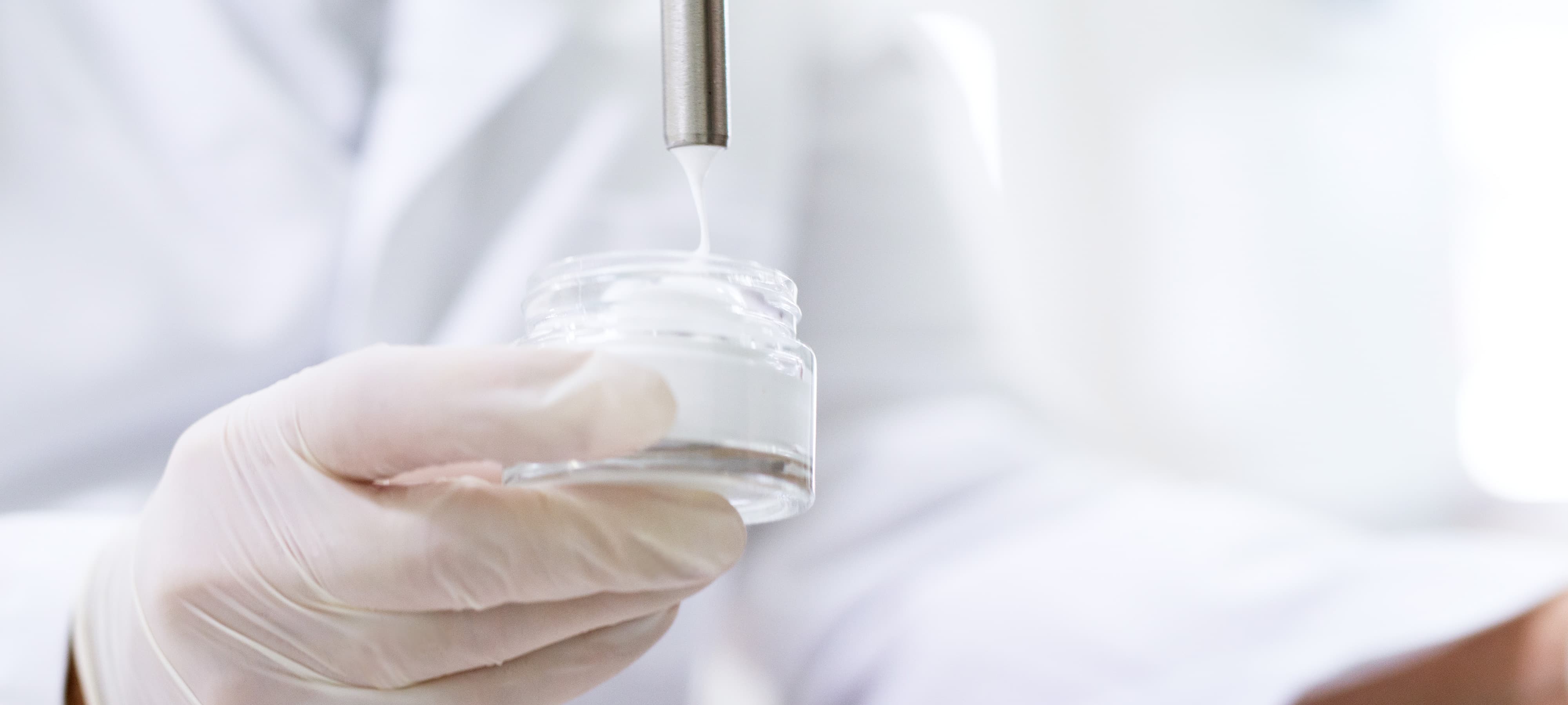 Nahaufnahme: Labormitarbeiter füllt weiße Creme in Glastiegel ab