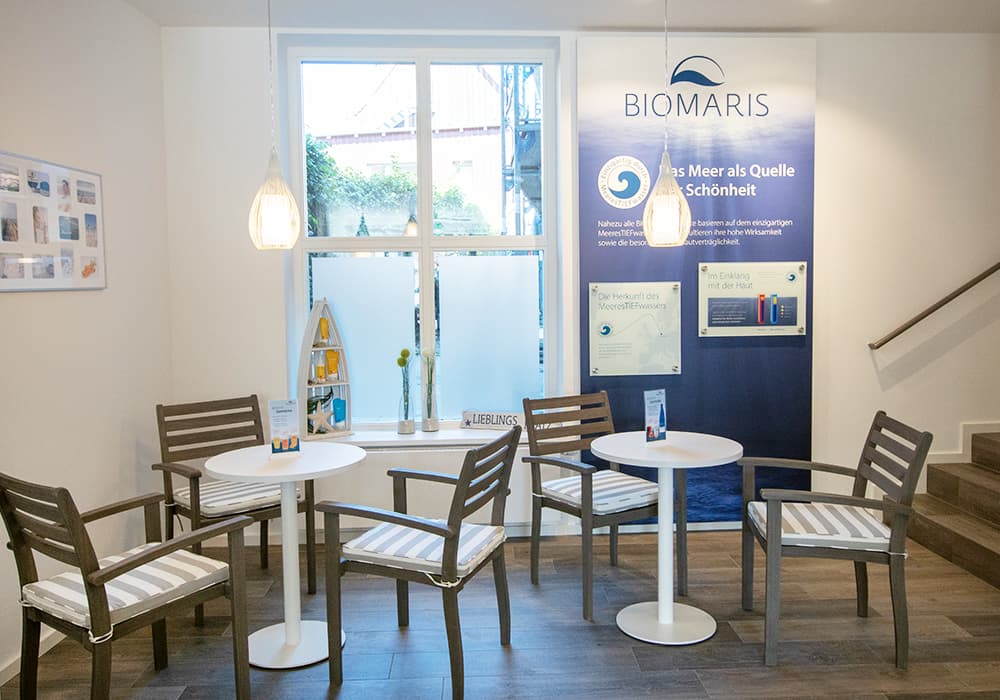 BIOMARIS Shop Travemünde Sitzbereich mit runden Tischen, Holzstühlen und BIOMARIS Infowand im Ladeninneren