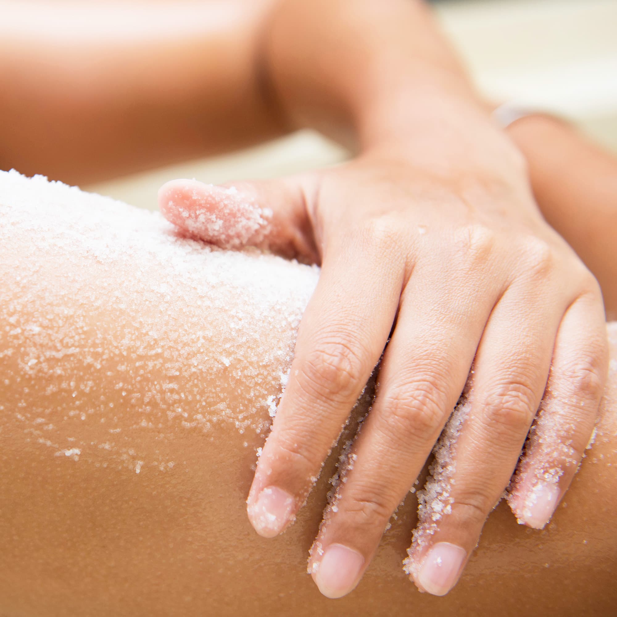 Hand massiert Peeling-Salz auf die Haut eines Oberschenkels