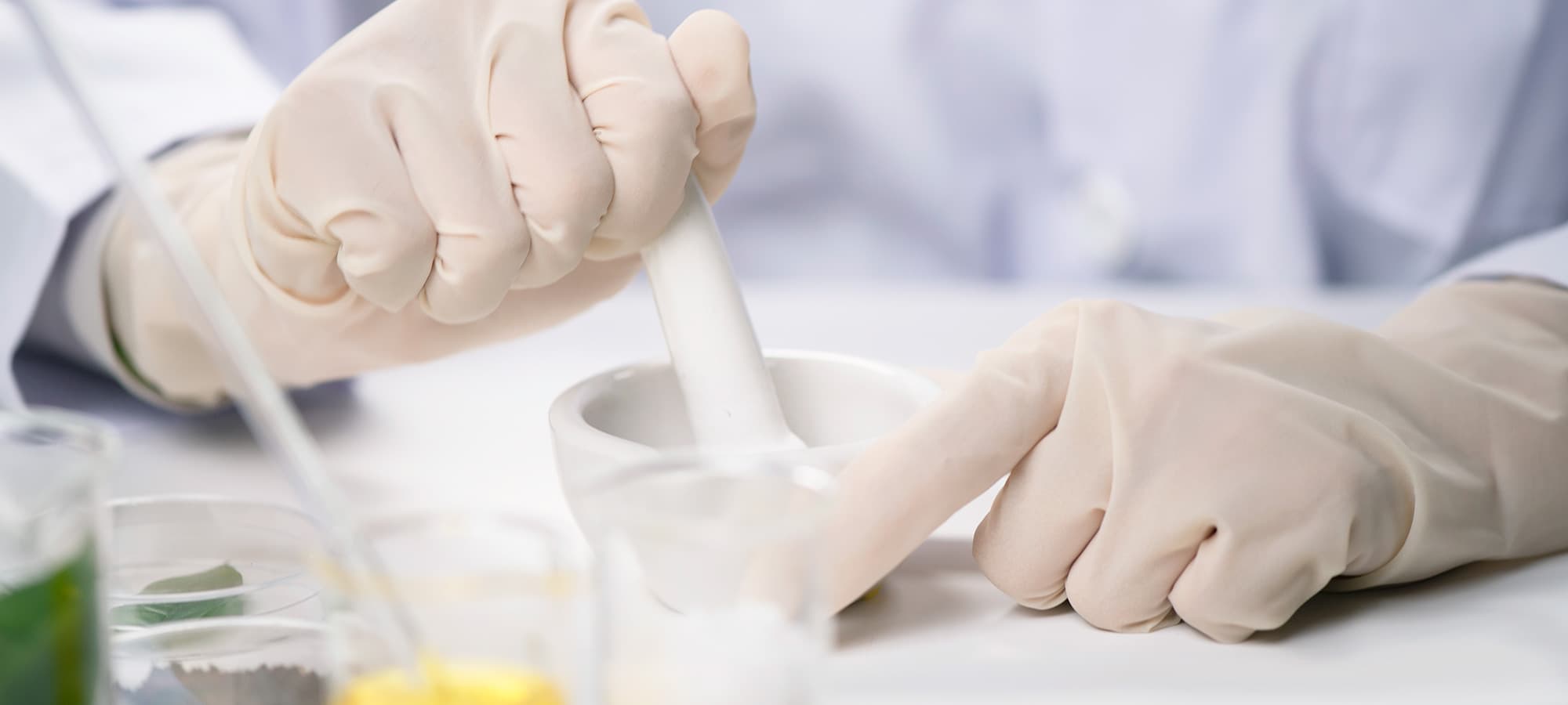 Labormitarbeiter in Handschuhen mischt Substanzen in einem Mörser