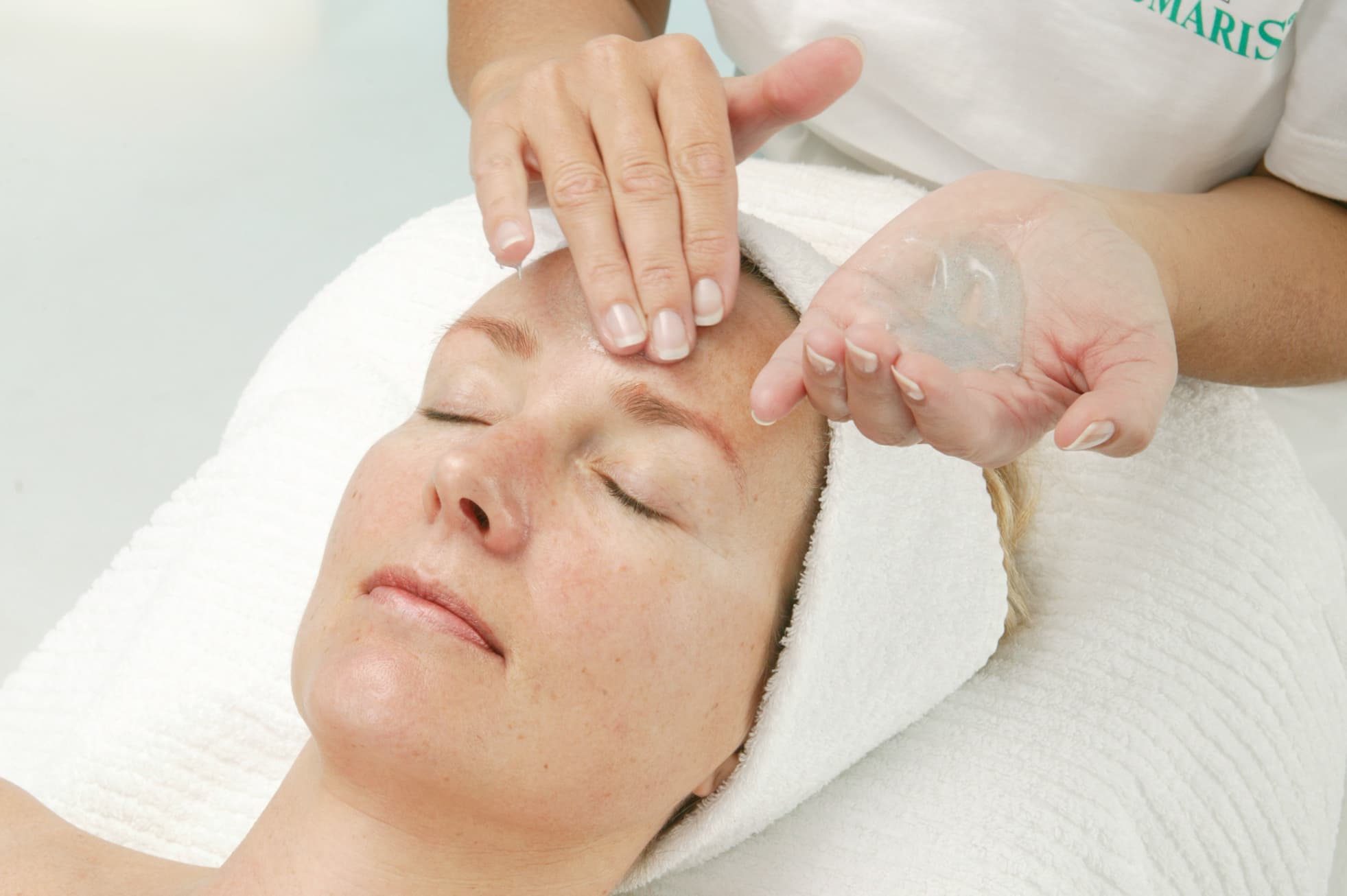 Gesichtsbehandlung Frau mit geschlossenen Augen erhält eine sanfte Gesichtsmassage mit Gel durch eine Kosmetikerin in einem Kosmetikinstitut.